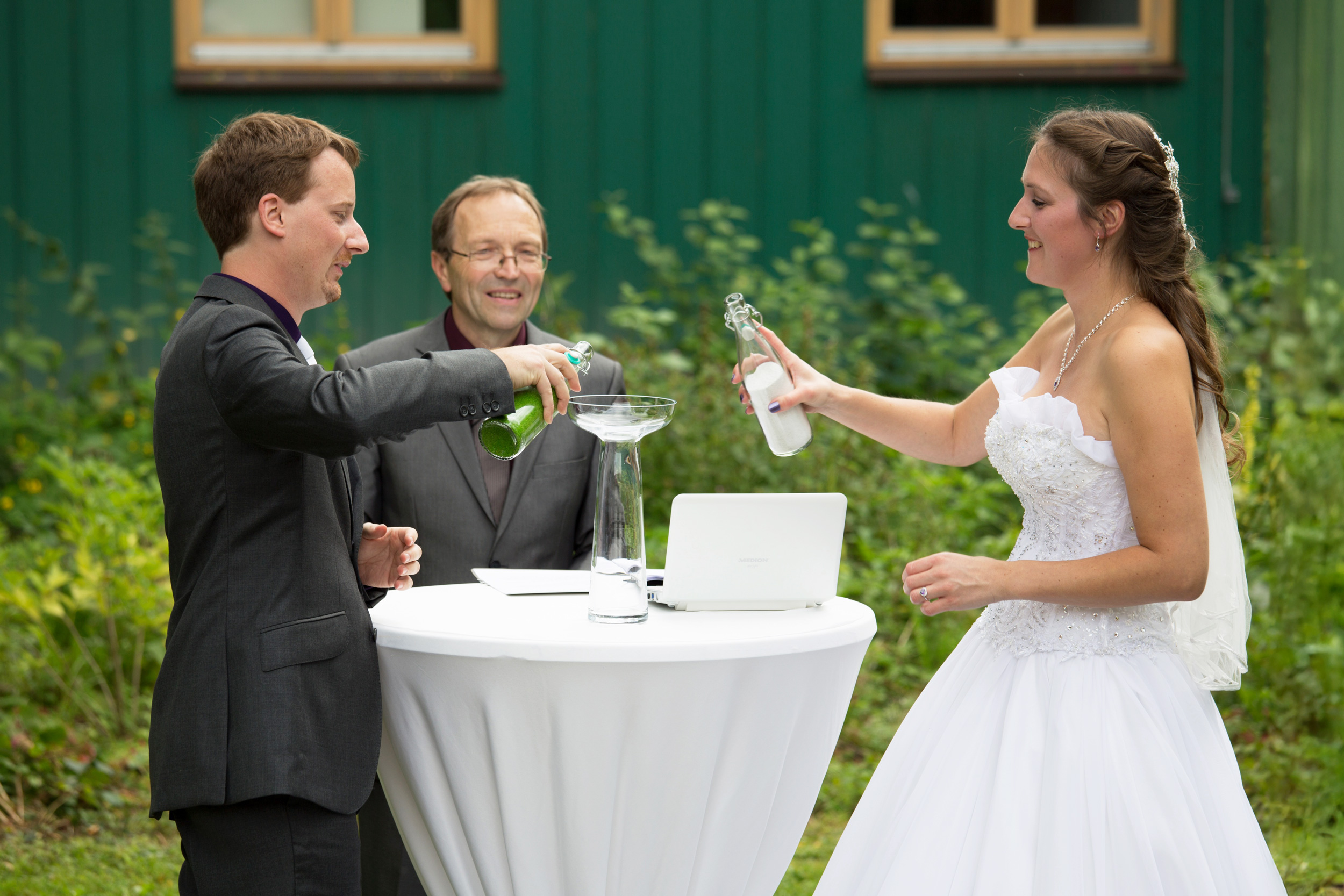 Hochzeitspaar beim Sandspiel. Freier Hochzeitssprecher in der Mitte lacht.